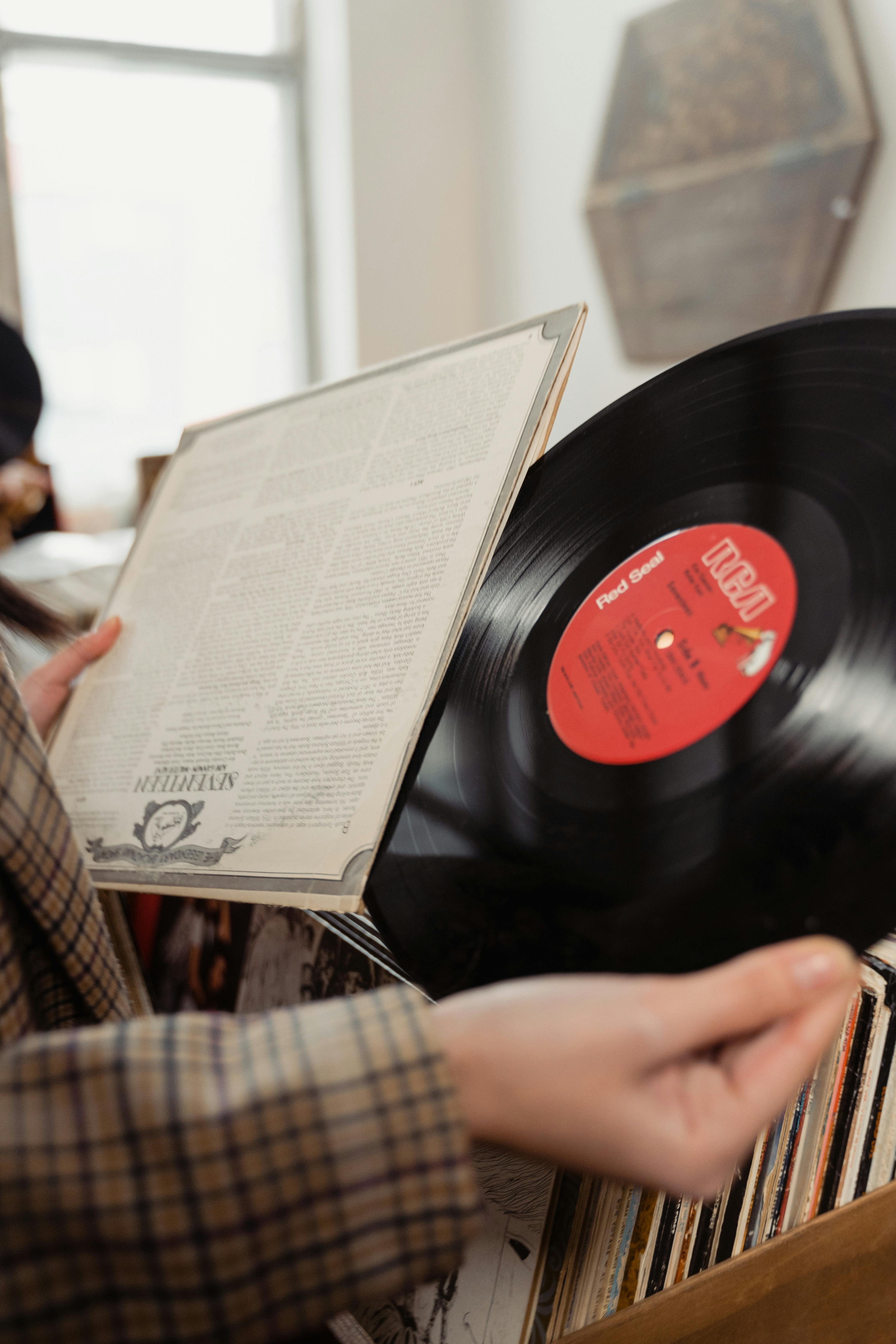 A person holding a vintage vinyl record and its cover indoors.